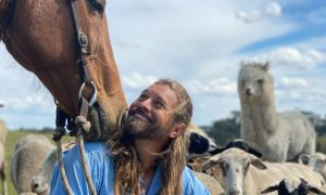 Farmer Dave (David Graham) smiling among his horse, alpacas and sheep on the farm