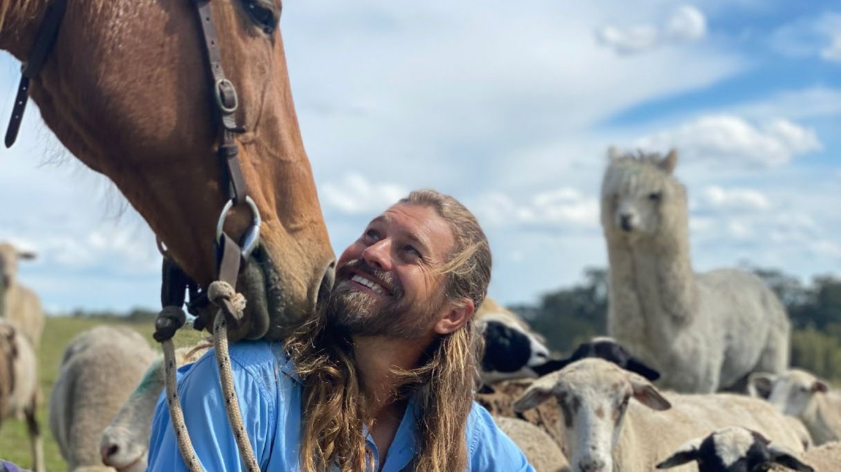 Farmer Dave (David Graham) smiling among his horse, alpacas and sheep on the farm