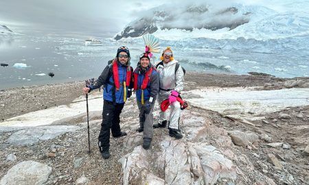 Antarctica Pride Cruise passengers on icy landscape with expedition ship in background