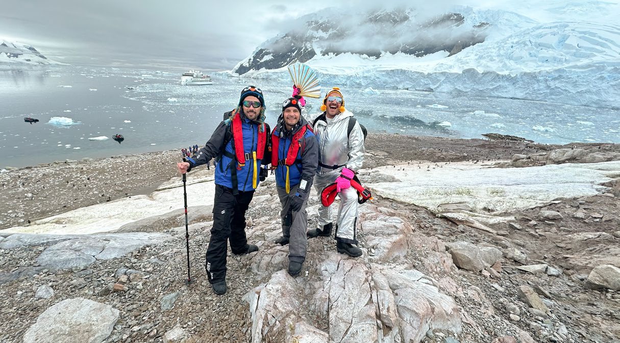 Antarctica Pride Cruise passengers on icy landscape with expedition ship in background