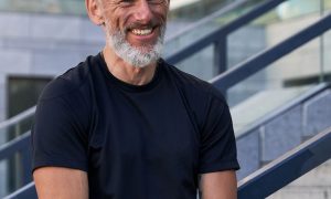 A fit man in a black t-shirt smiles on outdoor steps - physical and mental health