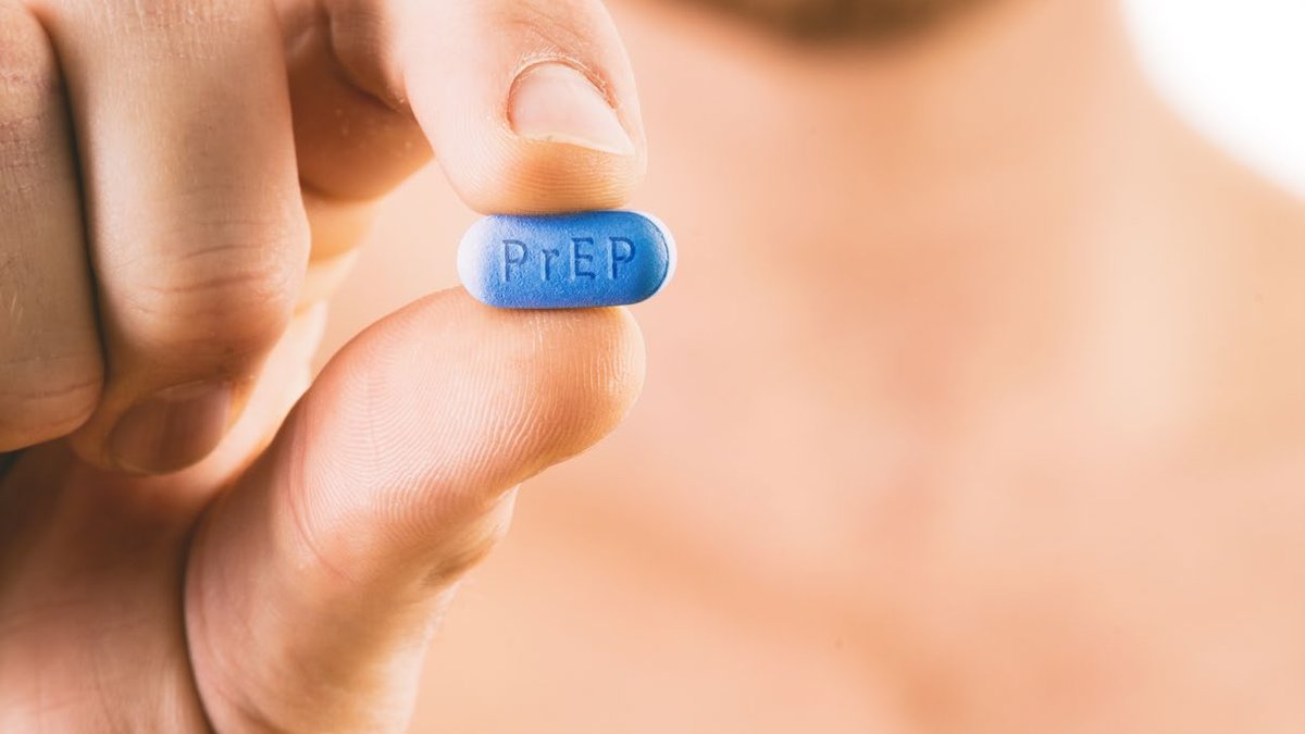 A man holds a blue PrEP pill between his fingers, face blurred in background