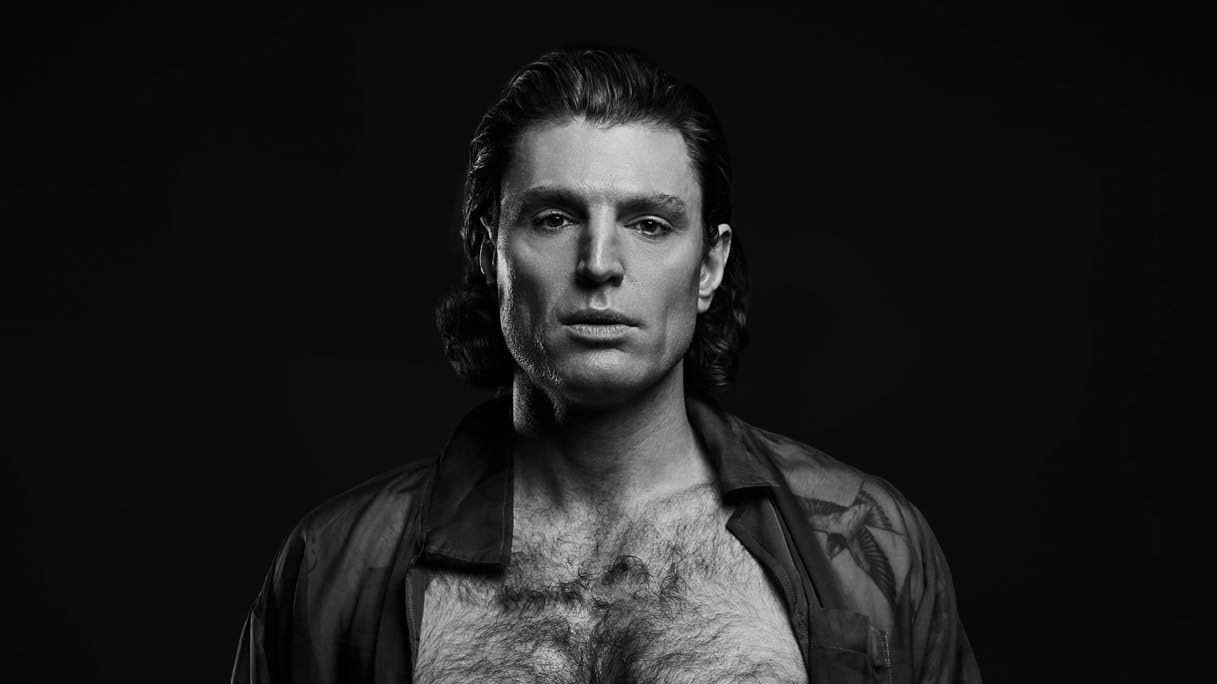 Reuben Kaye in a black and white studio portrait, open shirt, intense gaze